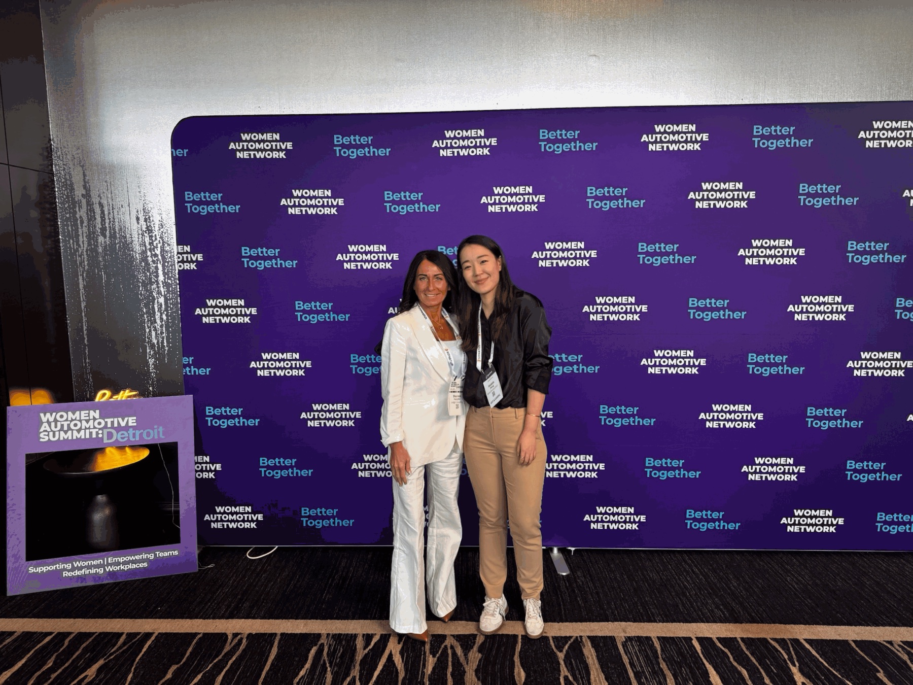 Two attendees at the Women Automotive Summit in Detroit, in front of the Women Automotive Network backdrop.